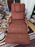 Front view of burgundy chaise-style recliner lounge chair showing upholstery, integrated footrest, headrest and wooden arms