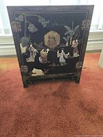 Front view of black lacquer cabinet with figural inlay and brass hardware