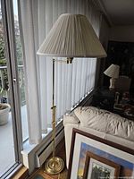 Full view of brass floor lamp with pleated shade beside sofa and window