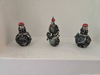 Front view of three glass snuff bottles with dragon metal overlays and red stoppers