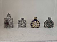 Front view of all four ornate metal-filigree perfume bottles showing shapes, finishes and decorative stones