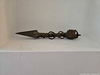 Side view of entire metal dagger showing blade, rings, and carved end.