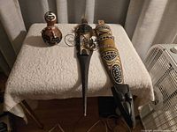 Three tribal decorative items on table: two wooden masks and one painted gourd