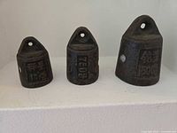 Front view of three cast-iron counterweights showing overall form, eyelet tops and raised weight markings