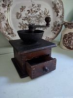 Front angle of wooden coffee grinder showing cast iron bowl, crank, and open drawer