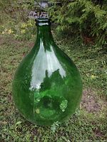 Large green glass demijohn bottle standing on grass