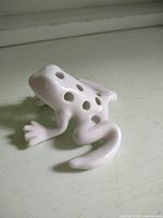 Overall view of white ceramic frog flower frog showing holes and form