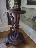 Full view of wood pedestal side table showing round top, carved supports and tripod base