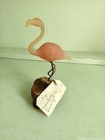 Front view of pink resin flamingo on wood base with tag