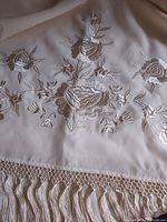 Close-up of floral embroidery and fringe on ivory satin shawl