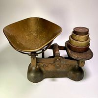 Front view of cast iron Avery scale with brass pan and stacked brass weights