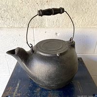 Full view of cast iron kettle showing wooden handle and swivelling lid