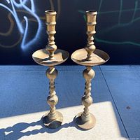 Full view of both tall brass candle holders standing side by side
