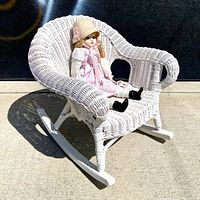 Front angle view of white wicker child rocking chair with doll for scale