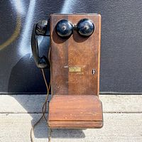 Front view of wooden wall telephone showing twin bells, handset, writing ledge