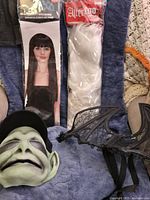 All four items arranged: black wig package, white wig package, alien mask with cap, bat wings