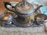 Overall view of teapot, creamer, sugar bowl on round tray atop rectangular tray
