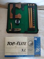 Open putting kit showing collapsible putter sections, wooden cup, ball and green felt case beside Top Flite ball box