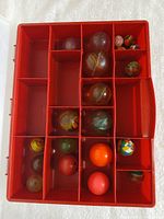 Red compartment case opened showing assorted bouncy balls inside