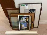 Group shot of six framed artworks and rolled print leaning against wall