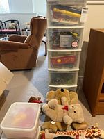 Tall clear organizer with multiple drawers containing toys, plush toys on floor