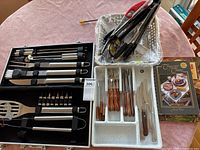 Overview of barbecue tool case, loose tongs in basket, cutlery tray with steak knives and forks, and cookbook