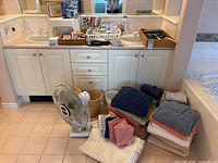 Overall view of towels, bathmats, fan, bins, stool, toiletries on vanity