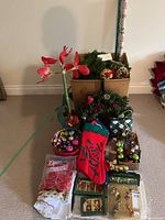 Group shot showing wreath, garland, wrapping paper roll, stocking, amaryllis stem, boxed ornaments and loose decorations