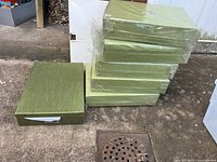 Stack of five green storage boxes with one additional box beside, showing lids