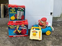 Group shot showing all four toys with two boxed items, music box and Mr. Potato Head with car
