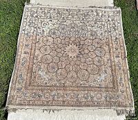 Full view of square oriental rug laid on grass and concrete