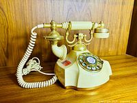 Full view of ivory and gold Electra Contessa rotary phone on wood surface