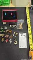 Overview of assorted earrings on mat with measuring tape and lot tag
