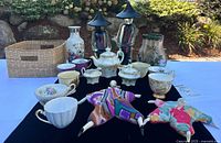 Lot overview showing china teacups, porcelain tea set, art glass vases, ceramic vase, wicker basket and Poupee Millet dolls