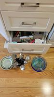 Drawer open showing assorted measuring tools and utensils with nested bowls and utensil holder on floor
