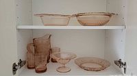 Cabinet view showing rectangular dish, round bowl, pitcher, four tumblers, compote, round plate