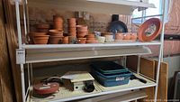 Shelving with terra cotta pots, saucers, plastic trays and heater visible