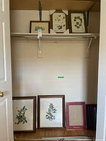 Overview of all framed prints and empty frames in closet