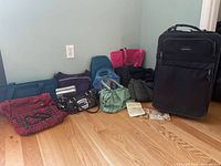 Group shot of all bags on floor including suitcase and handbags