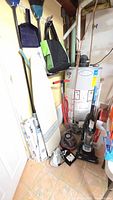 Overall view showing vacuum, polisher, ironing board, brooms, sweater dryers stacked against wall