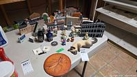 Overview of lot showing wood buildings, cat wall hanging, praying mantis plaque, vases, cat figurines and small decor on table