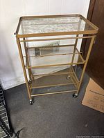 Full view of gold metal folding tea cart with glass top and two mesh shelves