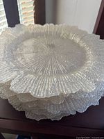 Stack of eight clear textured glass charger plates with ruffled edges