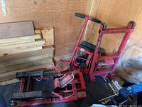 Two red Motomaster hydraulic motorcycle jacks leaning against wall