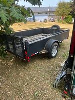 overall view of black single-axle utility trailer with ramp gate and deteriorated wood deck