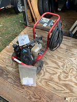 Full view of pressure washer on plywood floor with hose, manuals in bag