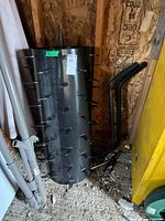 Black steel spiked drum aerator with hitch arms leaning nearby