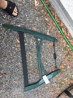 Full view of green wooden buck saw lying on gravel