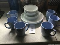 Full view showing six blue mugs surrounding stacked Corelle bowls and plates