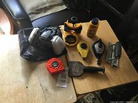 All items laid out on table showing respirator, tape measure, chalk line reels, chisel, iron, seam roller, bottle